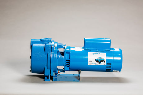 A blue industrial centrifugal pump with a motor, mounted on a metal base. The pump has cylindrical and rectangular components with a label on the side showing the brand. The background is a neutral gray.