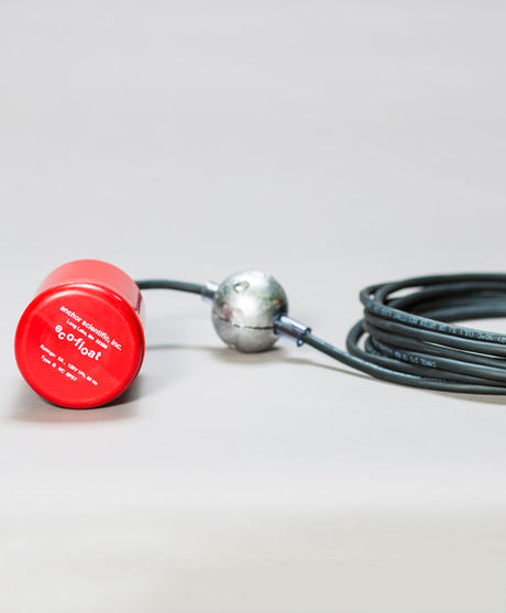 A red cylindrical float switch featuring a gray cable and metallic connector is set against a light gray background. The label shows "Eco-Float Red." This mercury-free level switch looks technical, likely designed for monitoring liquid levels.